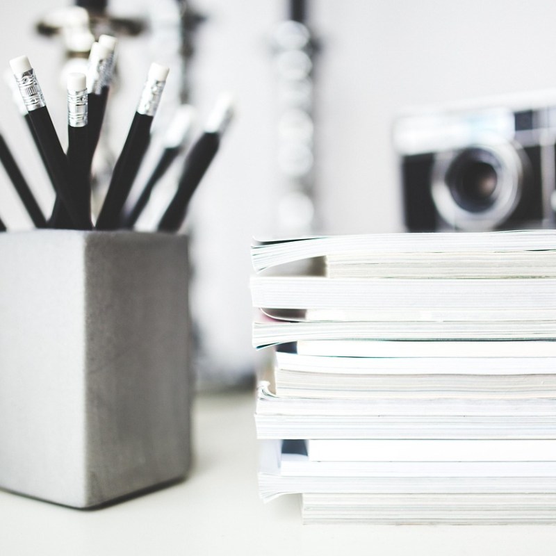 Pencils in a cup beside a stack of notebooks